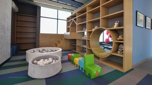 Un área de juegos infantiles con un amplio espacio de asiento circular, unidades de almacenamiento coloridas y una estantería de madera.