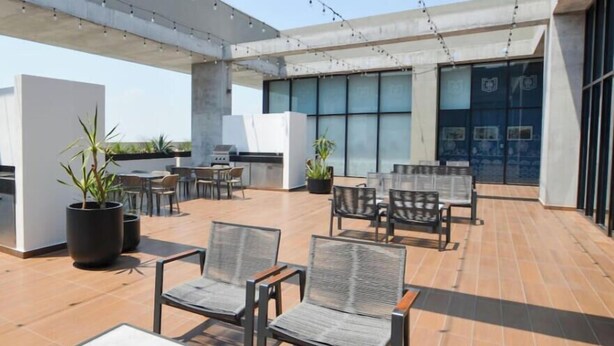 Un espacio al aire libre con patio, asientos, plantas en macetas y un diseño arquitectónico moderno.