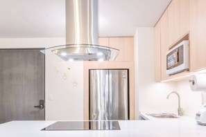 Eine moderne Küche mit einem Edelstahl-Kühlschrank, einer Glasküchenhaube, Holzschränken und einer Mikrowelle auf einem Regal.
