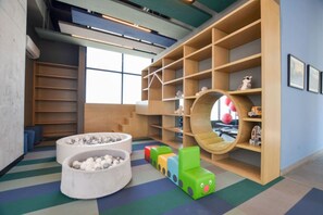 Ein Kinderspielbereich mit einer runden Sitzecke, bunten Bauklötzen und einem Bücherregal aus Holz.