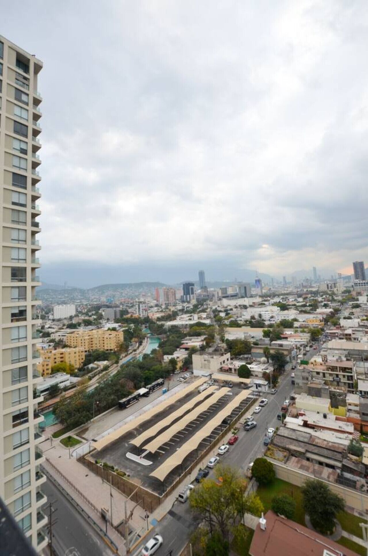 A high-rise building with a view of a cityscape, including a parking lot and various buildings.