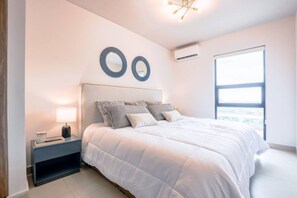 Une chambre à coucher comprenant un lit, une table de chevet, un miroir fixé au mur et une fenêtre.
