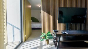 Un salon moderne avec un téléviseur, une plante et un lit à l’arrière-plan.