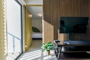 A modern living room with a TV, a plant, and a bed in the background. - ¡A pasos de Paseo Santa Lucía! 2 Camas Queen y Gym (Monterrey)