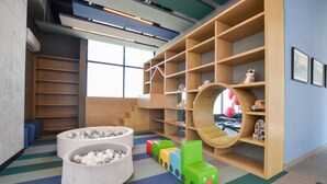 Un espace de jeux pour enfants avec un coin salon circulaire, des blocs de construction colorés et une bibliothèque en bois.