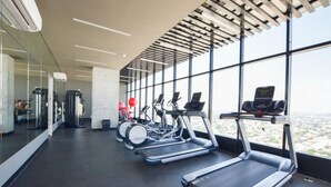 Une salle de sport équipée de tapis de course, de ballons d’exercice et offrant une vue sur la ville grâce à de grandes fenêtres.