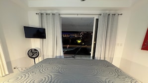Une chambre avec un lit, une télévision, un ventilateur et une vue sur l’extérieur.