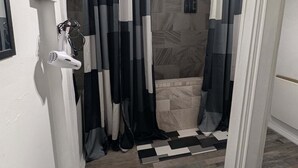 A bathroom with a shower, a hairdryer, and a patterned floor.