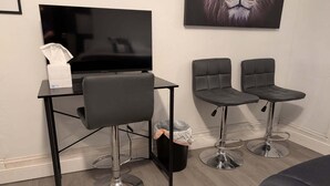 A room with a desk, two bar stools, a television, and a framed picture on the wall.