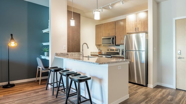 A modern kitchen with a central island, stainless steel appliances, and bar stools.