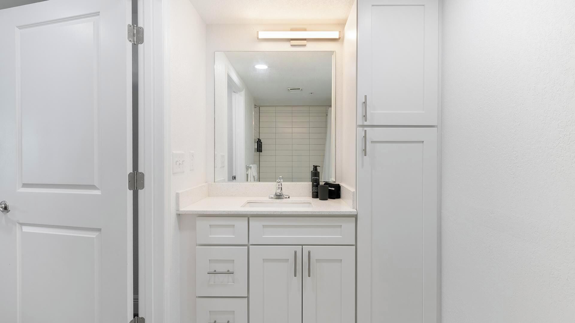 Un baño con muebles blancos, un espejo, un lavabo y una zona de ducha.
