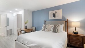 A bedroom with a bed, bedside tables, a desk, and a chair. - Landing Apartments Kissimmee - Celebration (Kissimmee)