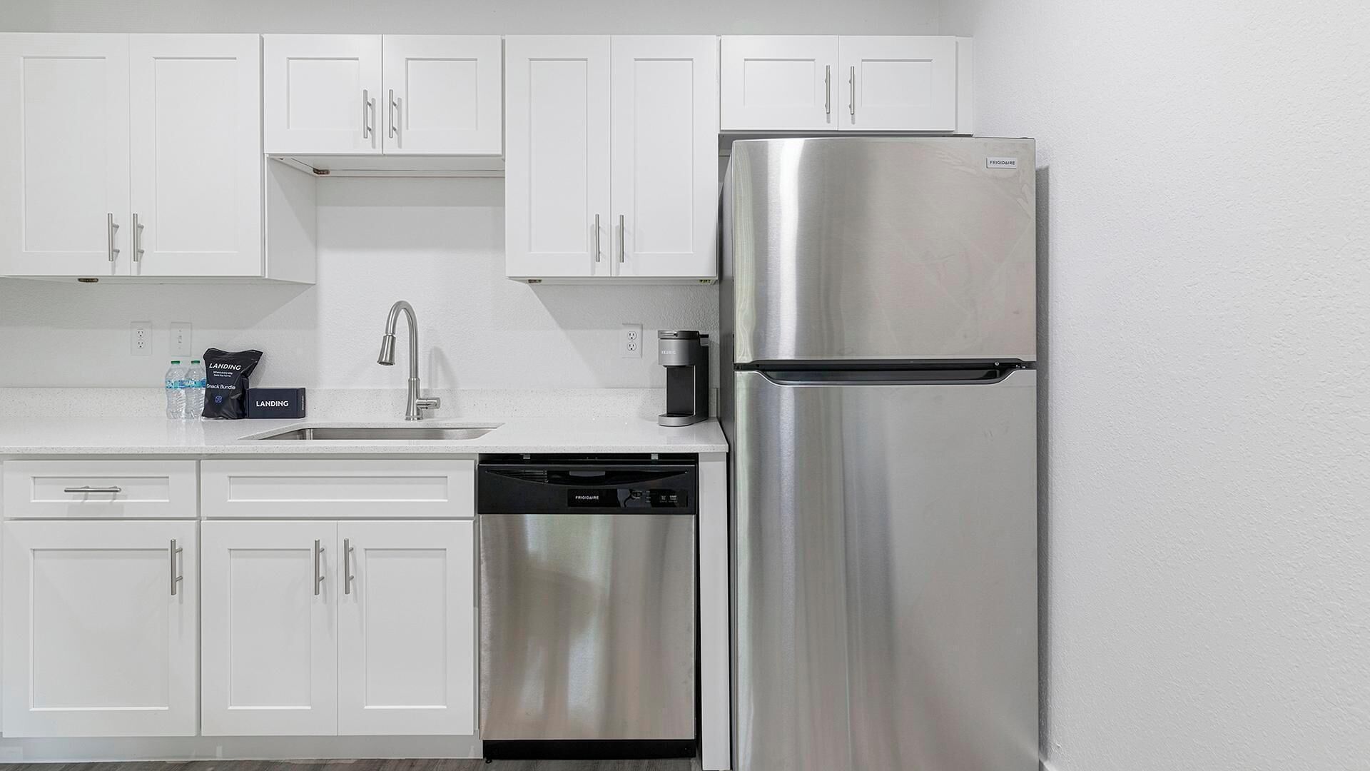 A kitchen with white cabinets, a stainless steel refrigerator, a dishwasher, and a coffee maker.