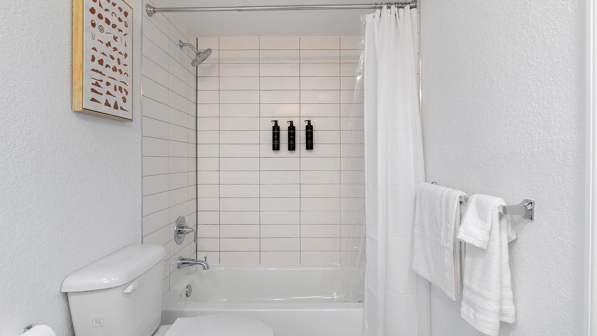 Un baño con inodoro, bañera, ducha y tres botellas negras en la pared.