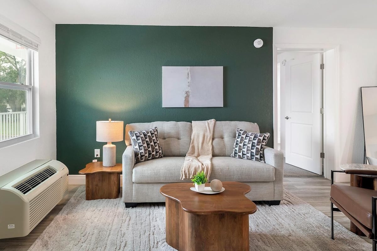 Un salon avec un mur vert, un canapé, une table basse, une lampe et un radiateur.