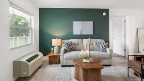 A living room with a green wall, a sofa, a coffee table, a lamp, and a radiator. - Landing Apartments Kissimmee - Celebration (Kissimmee)