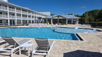 A pool area with lounge chairs, a building with multiple balconies, and a clear blue sky.
