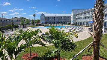 A hotel with a swimming pool, lounge chairs, and palm trees.