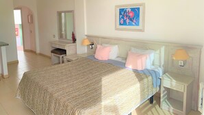 Un dormitorio con cama, mesitas de noche, cómoda, espejo y un cuadro en la pared.