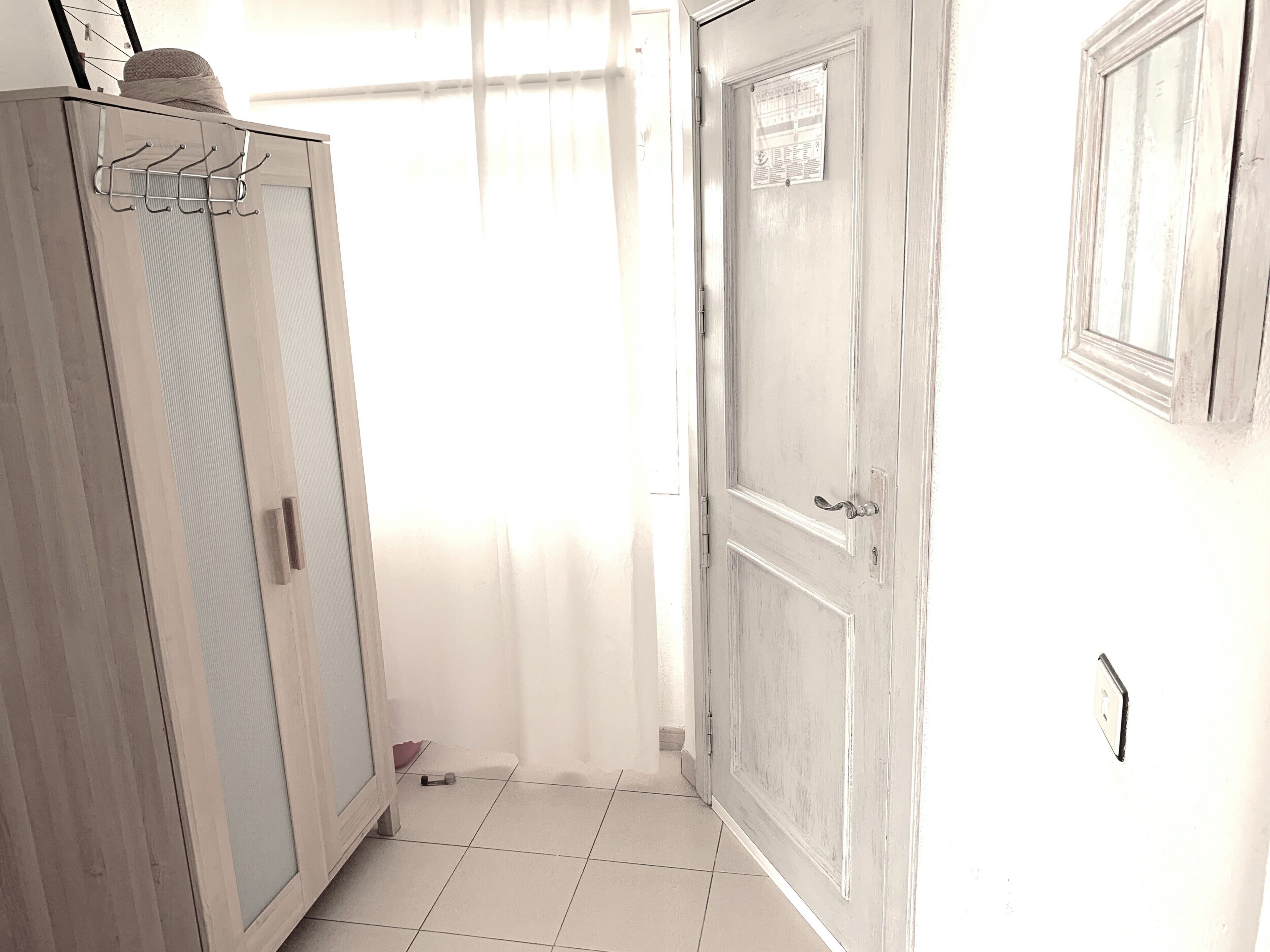 Un couloir avec une armoire en bois, une porte sur laquelle est affichée une note et un sol carrelé.