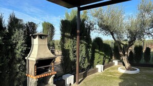 An outdoor barbecue grill with a chimney, surrounded by trees and a covered area.