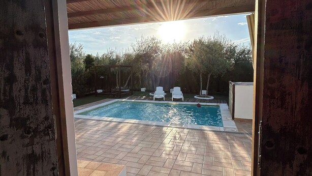 An outdoor swimming pool with a tiled deck, surrounded by trees and white lounge chairs.