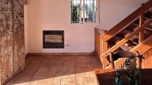 A spacious room with a wooden ceiling, a fireplace, a window, and a staircase.