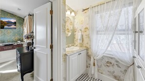 Une salle de bain avec un lavabo, un miroir et une fenêtre ornée de rideaux légers.