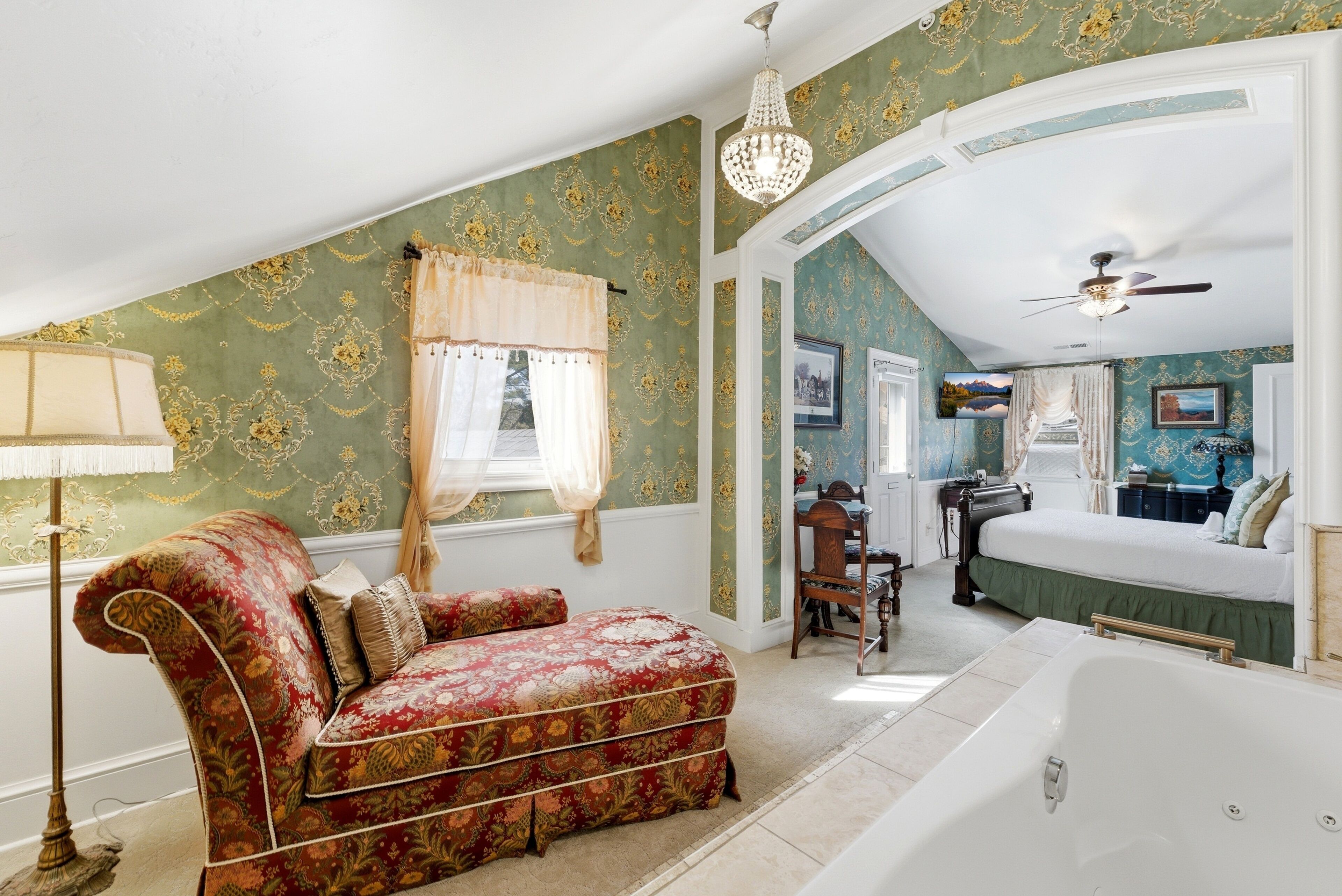 A bedroom with a large bed, a sitting area with a sofa, a desk, and a bathtub.