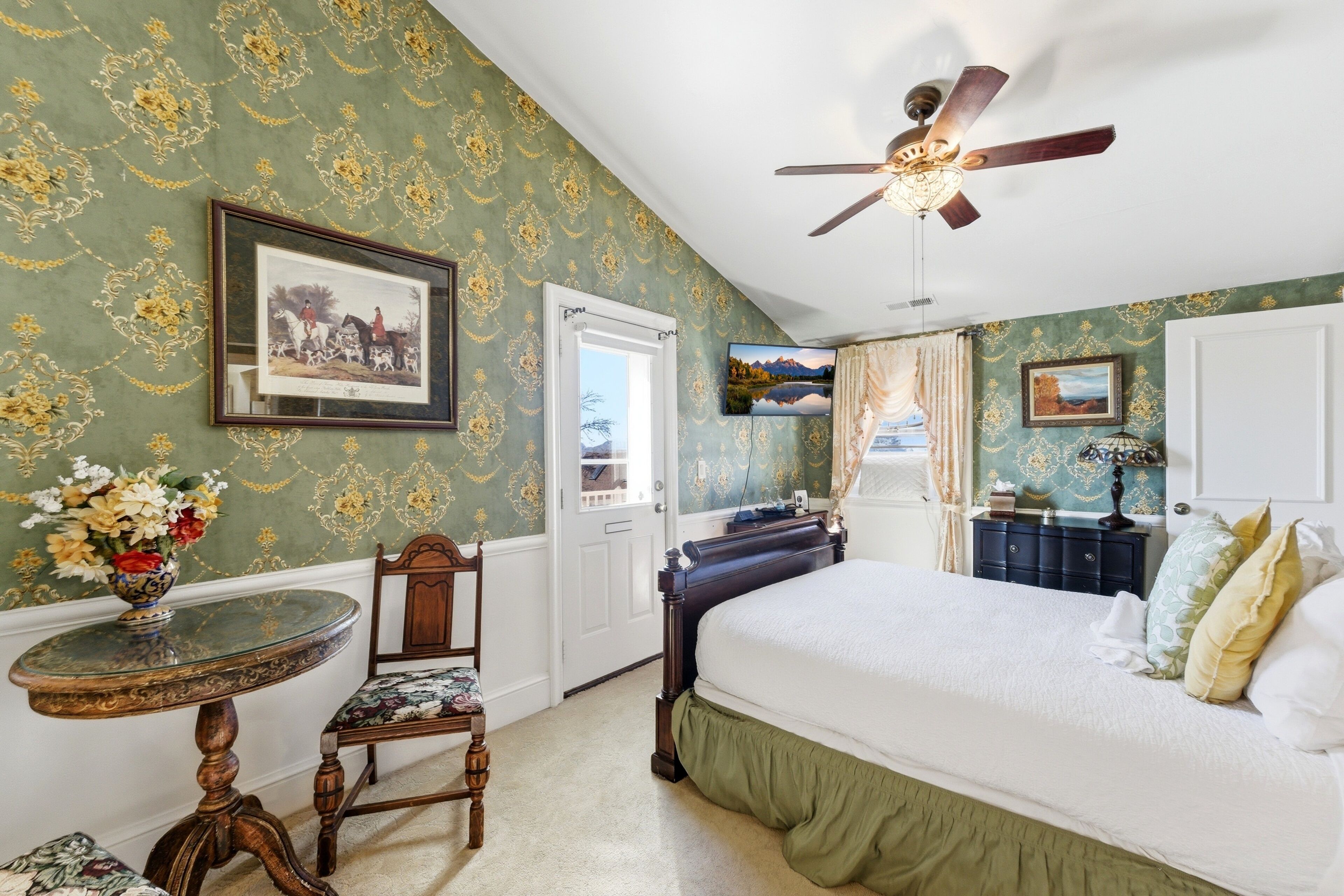A bedroom with a bed, a ceiling fan, a TV, a dresser, and a chair.