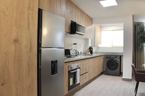 A modern kitchen with wooden cabinets, stainless steel appliances, a microwave, and a washing machine. - +MS +Única Suite +Inmejorable ubicación +Internet (Santiago de Querétaro)