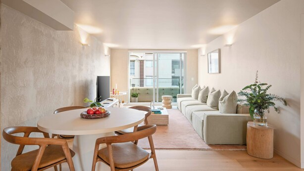 Una sala de estar moderna con una mesa redonda de comedor, sillas de madera, un sofá y una planta en maceta.