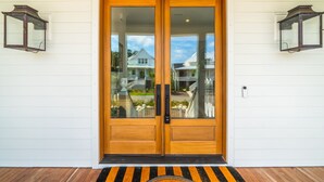A wooden double door with glass panels, a black doormat, and two wall-mounted lanterns. - 8311 Jack Island Dr – 4 BR / Walk to Spring House / Elevator + Screened Porch (Johns Island)