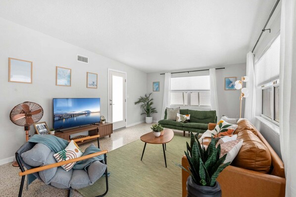 A living room with a television, sofa, coffee table, and a fan. - Beachside Boho Home. Fenced In Backyard & Short Walk to the Beach! 🌺🏖️ (Cape Canaveral)