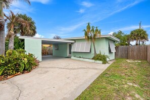 A single-story house with a covered garage, a fenced yard, and palm trees. - Beachside Boho Home. Fenced In Backyard & Short Walk to the Beach! 🌺🏖️ (Cape Canaveral)