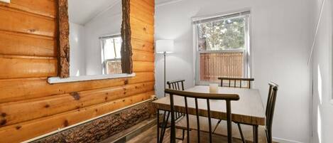 Una habitación con paredes de madera, una mesa de comedor con sillas, una lámpara y una ventana con persianas.
