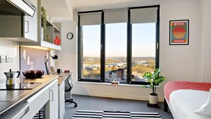 Una camera da letto moderna con una grande finestra, un letto, una scrivania e vista sulla città.