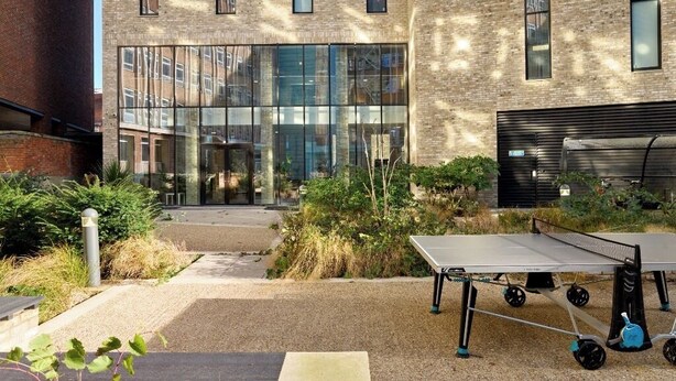 Spazio esterno con tavolo da ping pong, vialetto in ghiaia e un edificio con ampie finestre e pareti in mattoni.
