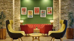 Una hall con parete in mattoni, un divano rosso, due poltrone gialle, un tavolino rotondo in legno e poster alle pareti.