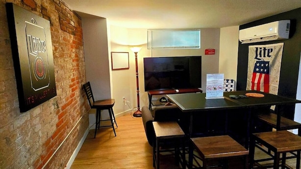 A modern living room with a brick wall, a flat-screen TV, a bar area, and an air conditioning unit.