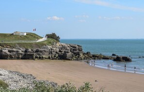 A coastal landscape with a sandy beach, rocky cliffs, and a building on a hill. - Pet friendly apartment in Royan with house sea view (Royan)