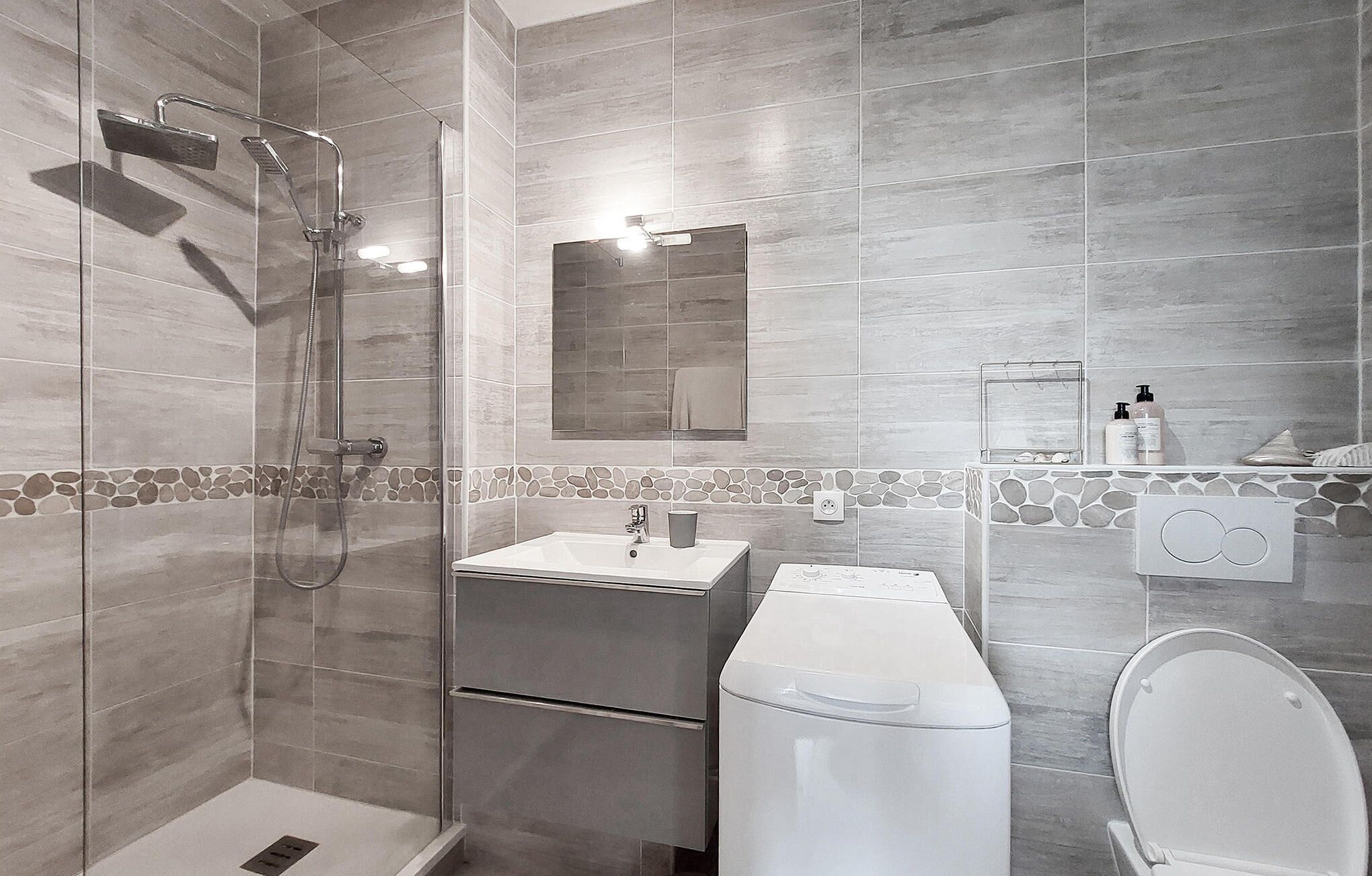 A modern bathroom with a glass shower enclosure, a white sink, a toilet, and a small mirror.