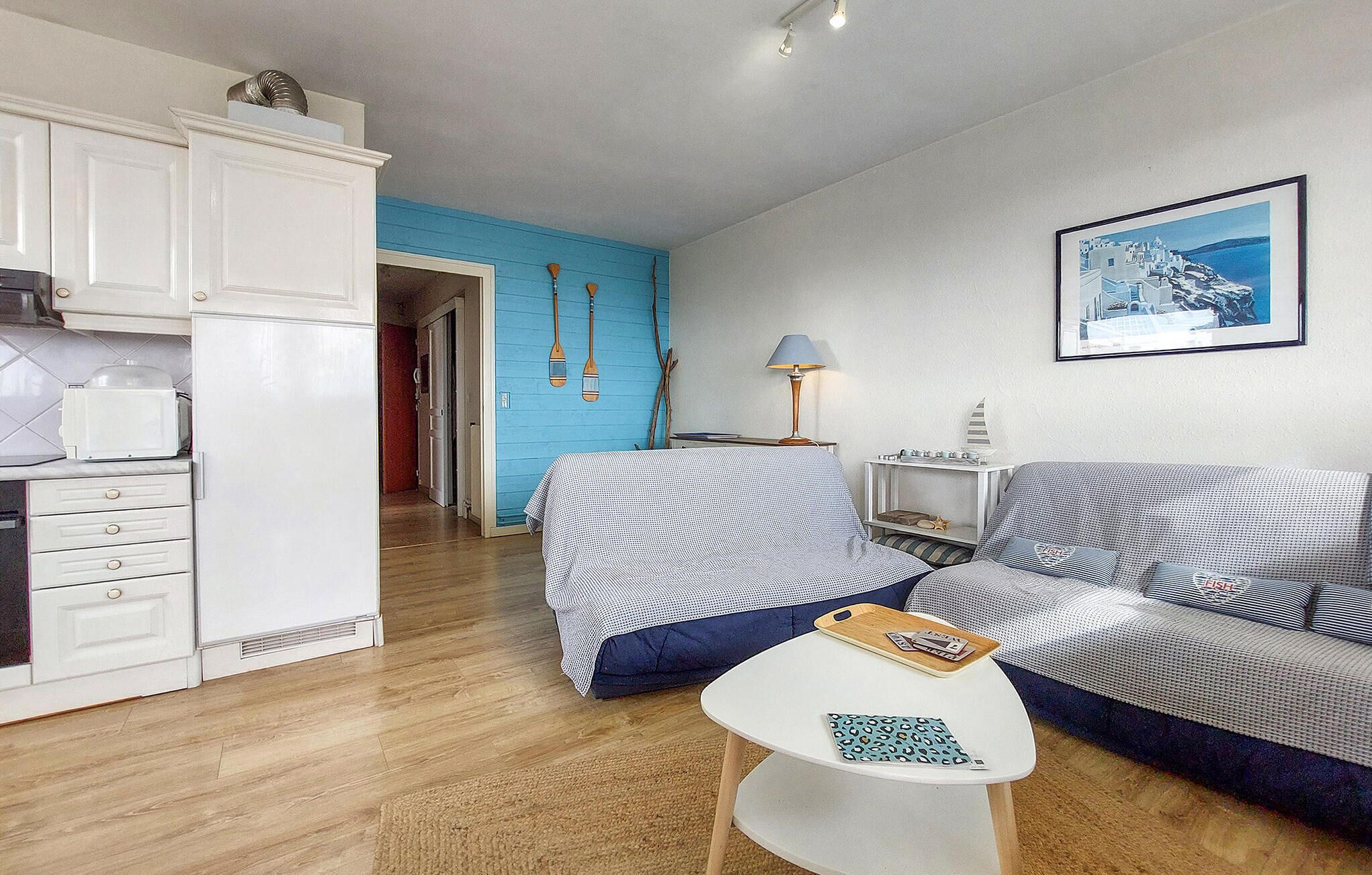 A compact living space with a kitchenette, a blue accent wall, a bed with striped bedding, a small table, and a framed picture on the wall.