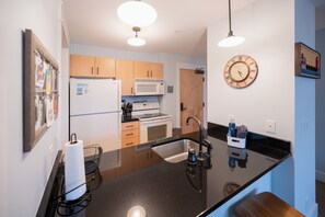 Une cuisine moderne avec des meubles en bois, un plan de travail noir, un évier en acier inoxydable et une horloge murale.