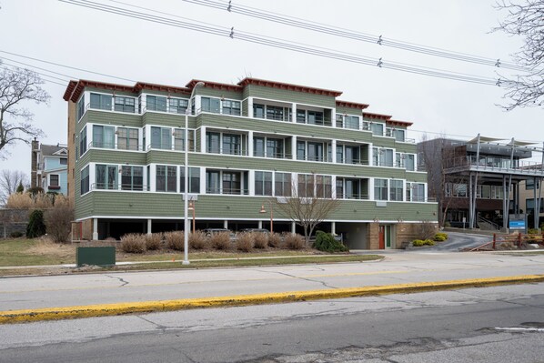 A multi-story building with a green facade, multiple windows, and a parking garage entrance. - Lake Michigan Condo | Walk to Downtown | Views + Parking (Grand Haven)