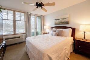 Une chambre à coucher comprenant un lit, deux tables de chevet avec des lampes, un ventilateur de plafond, un radiateur et une fenêtre avec des stores.