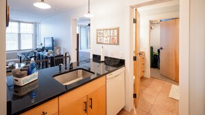 A modern kitchen with a black countertop, wooden cabinets, a dishwasher, and a sink. - Lake Michigan Condo | Walk to Downtown | Views + Parking (Grand Haven)