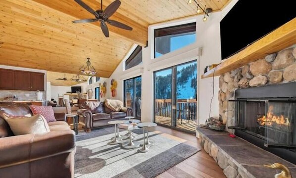 A spacious living room with a fireplace, wooden ceiling, and large windows. - Luxury 4BR Condo Near Diamond Peak & Lake Tahoe - Perfect for Families (Incline Village)