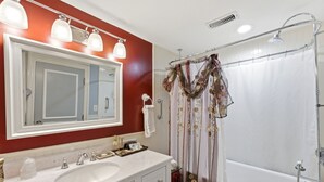 Un baño con lavamanos blanco, espejo doble y ducha con cortina estampada con motivos florales.