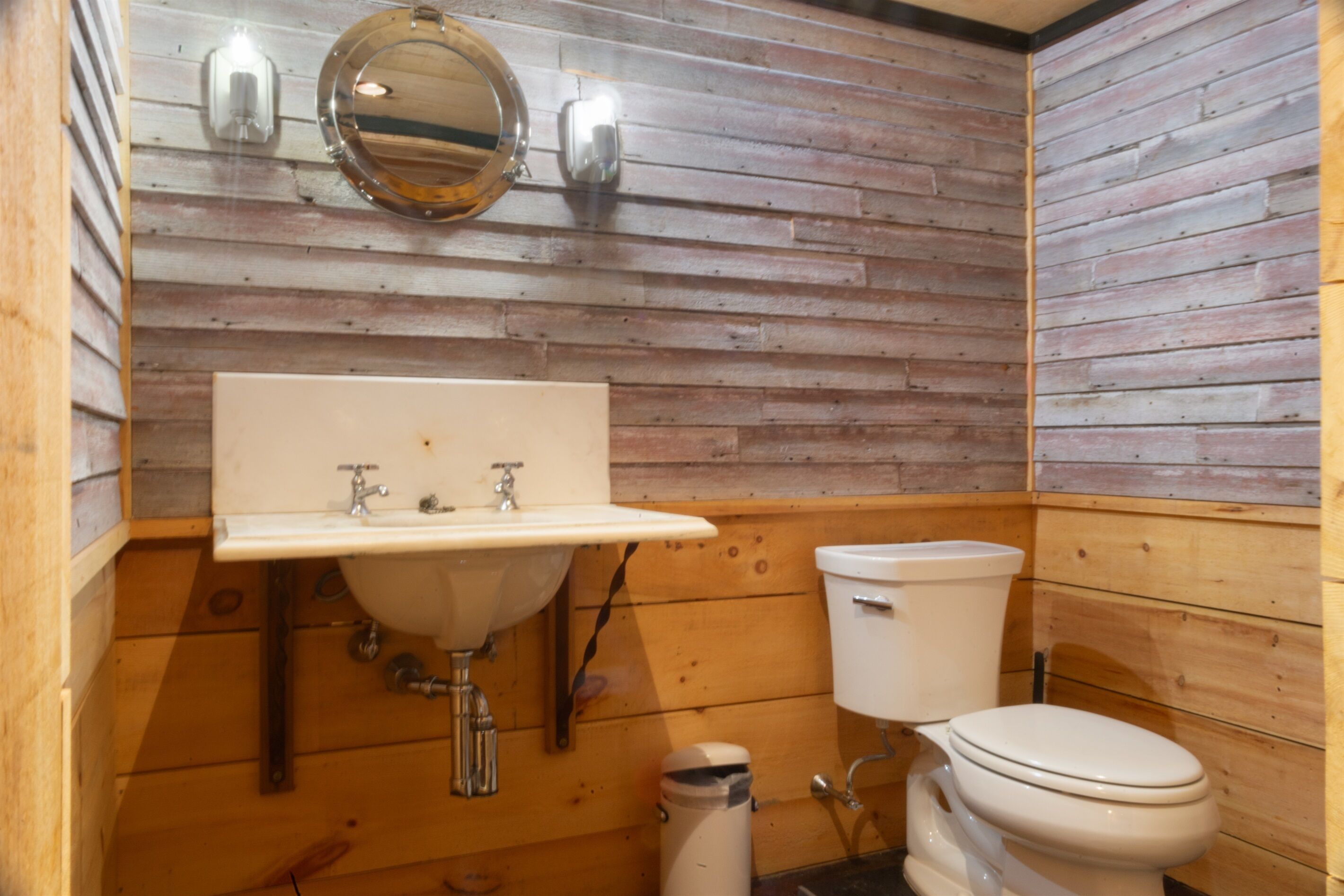 A wooden-paneled bathroom with a sink, toilet, and a mirror.